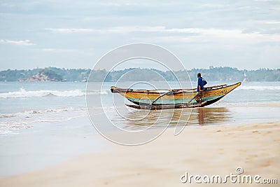 Weligama, Sri Lanka â€“ December 21, 2017: Alone fisherman resting near his boat after the night fishing in the morning time in W Editorial Stock Photo